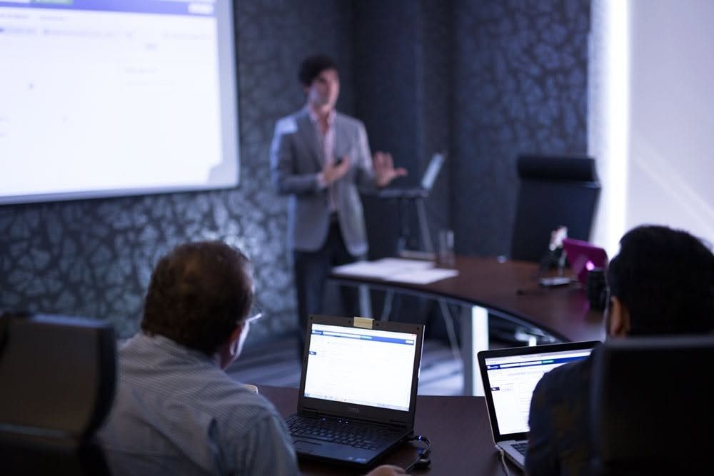 Armando J. Perez-Carreno presenting in front of a projector screen while attendees follow along on laptops