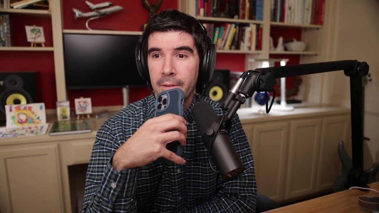 Armando J. Perez-Carreno in a dark plaid shirt holding up a phone while talking into a microphone on episode 43 of The Web Talk Show